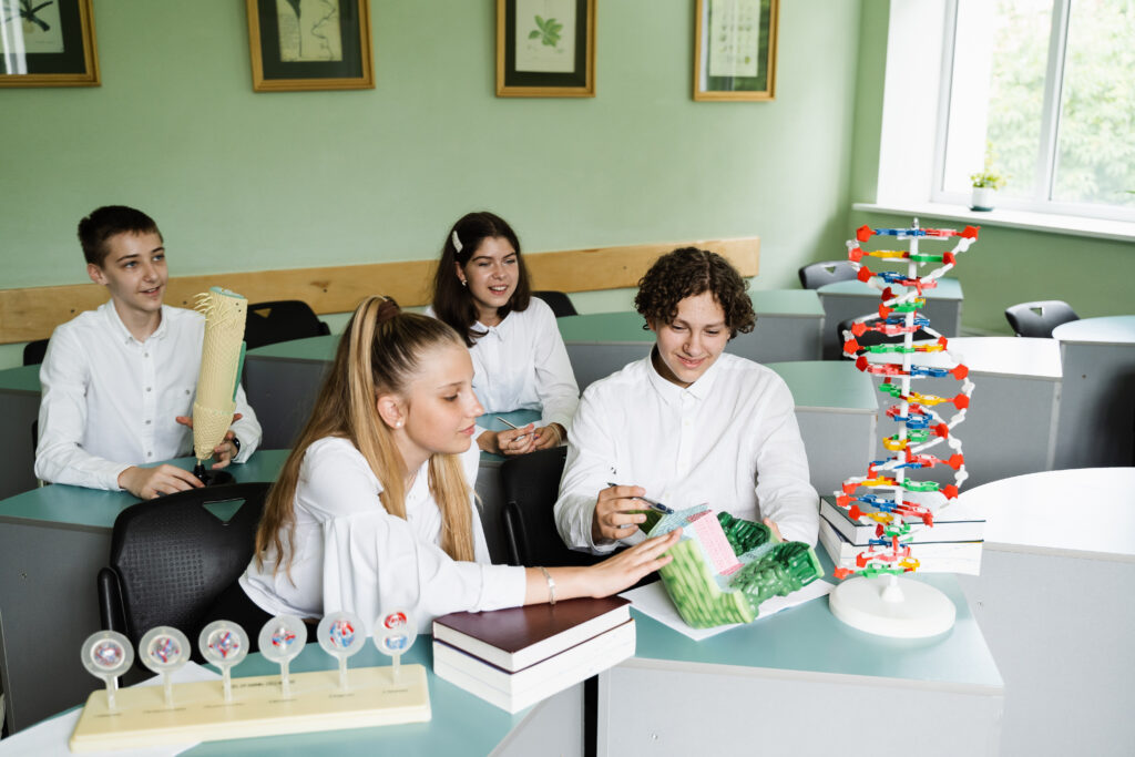 Pupils communicating and discussing in team at biology lesson at school with DNA and animal cell models on the table. Education at school of biology and chemistry.